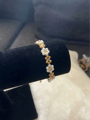 Pärlarmband med blommor i vitt och guld - Sött armband med små vita och guldfärgade pärlor formade som blommor. Armbandet har en tunn guldfärgad kedja och justerbar längd. 