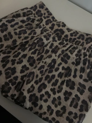 Leopardmönstrad kjol från Kappahl - Leopardmönstrad kjol från Kappahl i beige och svart. Kjolen har en bred resår i midjan och ett flowy fall som ger en snygg siluett. Perfekt för dig som vill sticka ut med ett djurmönster. Tillverkad i mjukt material för skön känsla.