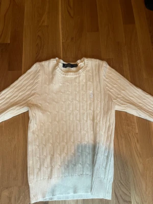 Vit kabelstickad tröja Polo Ralph Lauren - Super mjuk vit kabelstickad tröja från Polo Ralph Lauren med rund halsringning och diskret broderad logga på bröstet. Klassisk och tidlös design i mjukt material, perfekt för lager-på-lager och snygg till jeans eller kjol.