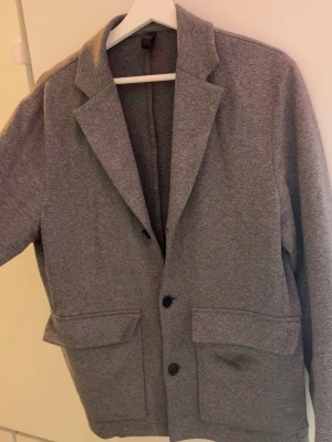 J lindberg blazer - Stilren grå kavaj med två knappar framtill och två stora fickor. Klassisk krage och mjukt material som ger en avslappnad look. Passar perfekt till både jeans och chinos för en snygg outfit. Originalpris 2199 mitt pris 599