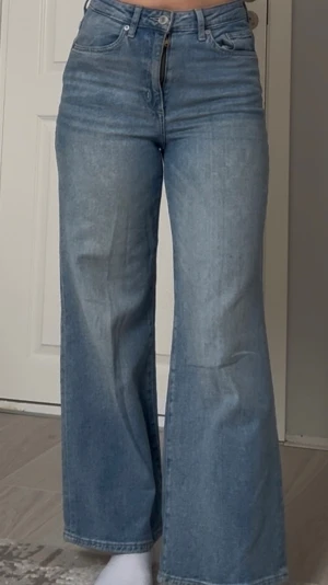Blåa vida jeans med hög midja - Säljer ett par ljusblå jeans med hög midja och vida ben. Jeansen har klassisk femficksdesign och stängs med dragkedja och knapp. Perfekta för en avslappnad och trendig look.