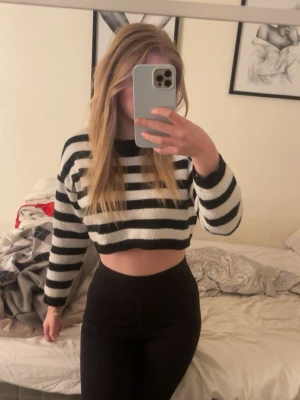 Randig cropped stickad tröja - Säljer en svartvit randig cropped stickad tröja med långa ärmar och rund hals. Tröjan har breda horisontella ränder och ribbstickade muddar vid ärmslut och nederkant. Perfekt för en trendig och avslappnad look. Från Shein i storlek S.