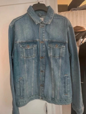 Klassisk blå jeansjacka - Snygg blå jeansjacka från Initz med raka linjer och klassisk krage. Jackan har två bröstfickor med lock och knapp samt två sidofickor. Stängs med metallknappar framtill och har en avslappnad passform. Perfekt för en cool och tidlös stil.