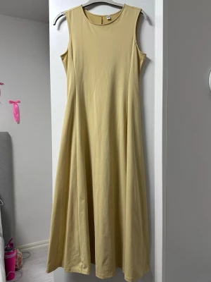 Gul ärmlös långklänning - En enkel och stilren gul långklänning i mjukt bomullsmaterial. Klänningen är ärmlös med rund halsringning och har en rak, luftig passform som faller snyggt. Perfekt för varma dagar och lätt att styla med accessoarer.