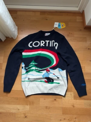 Lyxig stickad tröja från MC2 saint barth med tryck av cortina. - Riktigt stilig stickad tröja från saint barth för de som vill sticka ut bland mängden, plagget är sprillans nytt och helt oanvänt. Tröjan är i riktigt fint material och passformen är dunder. Tröjan har tryck av den italienska staden Cortina där OS i skidor utspelat sig. Produktbeskrivningen hittar du på sista bilden i profilen där det står mer detaljer om materialet och så vidare.