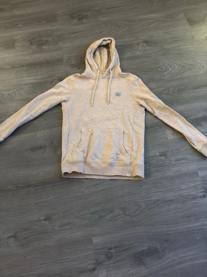 Beige hoodie med ficka framtill - Snygg beige hoodie med huva och dragsnören. Hoodien har en stor magficka framtill och ribbade muddar vid ärmslut och nederkant. Perfekt för en avslappnad stil och enkel att matcha med jeans eller joggers.