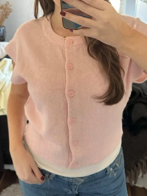 Ljusrosa stickad topp  - Supersöt ljusrosa kofta med korta ärmar och rund hals. Koftan har knappar framtill i matchande färg. Perfekt till sommaren. Storlek M, aldrig använd med prislapp från Nelly💕