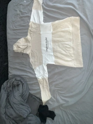 Beige och vit hoodie med tryck - Säljer en beige och vit hoodie från Jack and Jones med patchwork-design och tryck på bröstet. Hoodien har dragsko i huvan och är tillverkad i mjukt bomullsmaterial. Perfekt för en chill och avslappnad stil.