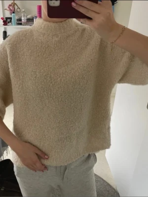 Trekvarts stickad tröja - Mysig beige stickad tröja med boxy passform och kortare ärmar. Tröjan har en högre rund halsringning och är gjord i ett fluffigt, mjukt material som känns skönt mot huden. Perfekt för lager på lager och chill dagar.