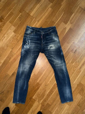 Blå  jeans från Dsquared2. Storlek 48. - Säljer ett par blå jeans från Dsquared2 med slitningar, färgstänk och en snygg tvättad look. Jeansen har raka ben, klassisk femficksmodell. Nypris var cirka 4600. 