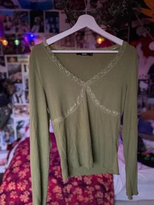 Olivgrön ribbad topp🫒 - Olivgrön långärmad topp från Bik Bok med stretchigt material och spetsdetaljer längs v-kragen och bröstet. ‼️Fråga om mått/om du vill se den på‼️.                     Den har lite smink stains i bilden fast de går bort i tvätten/den tvättas såklart innan skickas.