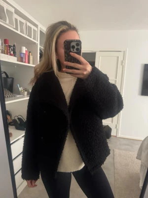 Svart teddyjacka med oversized passform - Mysig svart teddyjacka med oversized passform och stora ärmar. Jackan har en fluffig struktur och är perfekt för kalla dagar. Enkel design utan synliga loggor eller detaljer. Passar dig som gillar en avslappnad och trendig stil.