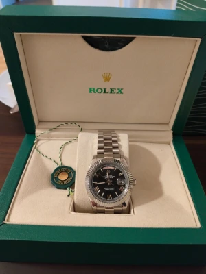 Klocka med svart urtavla - Använd ett fåtal gånger, mycket fint skick och tickar på som den ska. Låda och påse + papper medföljer