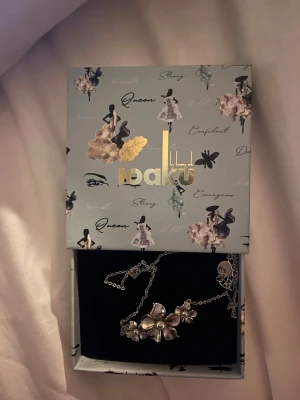 Halsband från Ioaku - Säljer ett elegant halsband från Ioaku med silverfärgade blommor som hängsmycke. Kedjan är tunn och smidig, och blommorna har en snygg metallisk finish. Perfekt för dig som gillar unika accessoarer med naturinspirerad design. Orginalpris 499