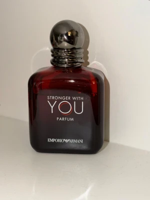 Emporio Armani Stronger With You Parfum - Emporio Armani Stronger With You Parfum i en mörkröd, fyrkantig glasflaska med rund, silverfärgad kork. Flaskan har elegant vit text och en stilren design som känns lyxig och modern. Perfekt för dig som gillar exklusiva dofter och snygga flaskor.