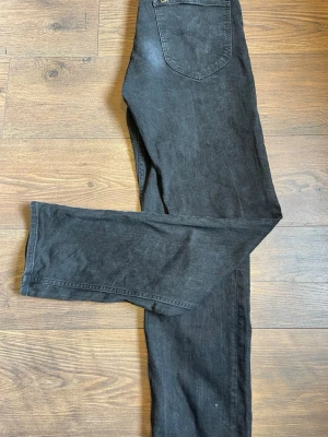 Svarta raka jeans från Lee - Säljer ett par svarta jeans från Lee med klassisk femficksmodell och raka ben. Jeansen har normal midja och är tillverkade i ett mjukt denimtyg som ger en avslappnad look. Perfekta för dig som gillar en enkel och tidlös stil.