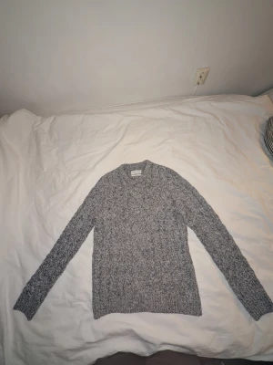 Gråmelerad stickad tröja - Säljer en gråmelerad stickad tröja från Pier One med rund halsringning och långa ärmar. Storlek Medium. Använd ca 5 gånger. Mannen på bilden är 187 cm lång.