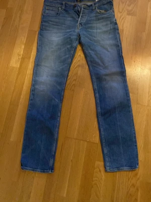 Blå raka Lee jeans med klassisk tvätt - Snygga blå Lee jeans med rak passform och klassisk tvätt. Jeansen har fem fickor och subtila slitningar framtill för en avslappnad look. Perfekta till en enkel t-shirt eller hoodie. Obs saknas ett par knappar i gylfen. 