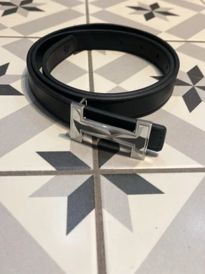 Svart skärp med silverfärgat H-spänne - Pris kan diskuteras!!! Snyggt svart skärp med ett stilrent H-format spänne i silverfärg. Skärpet är smalt och tillverkat i skinn, perfekt för att lyfta vilken outfit som helst. Passar både till jeans och kostymbyxor för en clean look.
