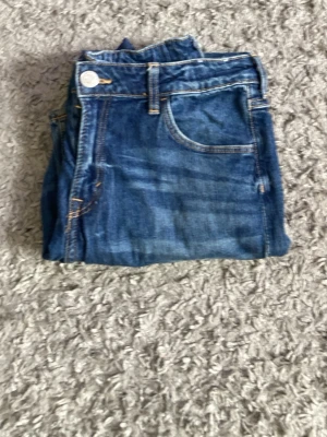 Blå raka jeans med klassisk passform - Snygga blå jeans i klassisk modell med raka ben och fem fickor. Jeansen har tydliga kontrastsömmar och silverfärgade knappar. Perfekta för en avslappnad och trendig look.