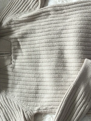 Beige ribbstickad tröja - Säljer en beige ribbstickad tröja med lång ärm och rund hals. Tröjan har en mjuk och stretchig känsla med horisontella ränder i stickningen. Perfekt för lager på lager och enkel att matcha med olika outfits.