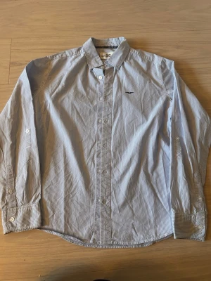 Blårandig skjorta från Hampton Republic - Klassisk blårandig skjorta från Hampton Republic med vit knappstängning och liten broderad logga på bröstet. Skjortan har lång ärm, krage och är tillverkad i mjuk bomull. Perfekt för en clean och stilren look.