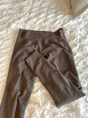 Impact leggings från DFYNE - Säljer ett par bruna seamless leggings från DFYNE med hög midja och stretchigt material. Perfekta för träning eller chill, med diskret logga vid linningen. Sitter tight och formar sig efter kroppen för en snygg siluett. Helt nya, använd 1 gång, säljer då de är för små 