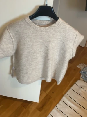Beige stickad tröja Gina Tricot - Beige stickad tröja från Gina Tricot med kort ärm och rund halsringning. Tröjan har en mjuk och lite lös passform, perfekt att styla med jeans eller kjol. Materialet känns mysigt och passar bra till lager-på-lager.