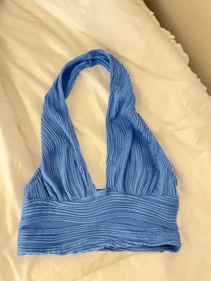 Blå ribbad halterneck linnetopp - Säljer en blå ribbad linnetopp med halterneck och djup urringning. Toppen har en croppad passform och är tillverkad i ett mjukt, stretchigt material. Perfekt för sommarens alla outfits!