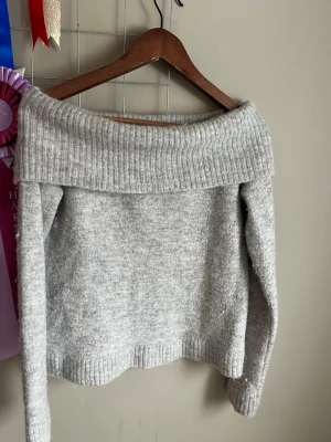 Ljusgrå off shoulder stickad tröja - Mysig ljusgrå stickad tröja med bred off shoulder-krage och långa ärmar. Tröjan har ribbstickade muddar vid ärmslut och nederkant.