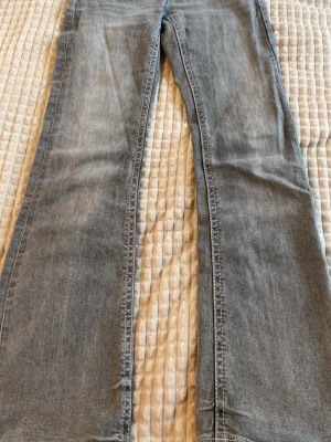 Grå bootcut jeans med fickdetaljer - Säljer ett par grå bootcut jeans med snygga fickdetaljer bak och dekorativa knappar. Jeansen har en klassisk femficksmodell och är tillverkade i mjukt denimtyg. Perfekta för dig som gillar en avslappnad men trendig look. Är använda men fortfarande bra skick. Pris kan diskuteras🫰🏻