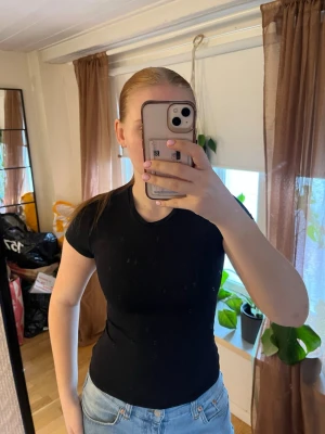 Svart tight t-shirt från H&M - En klassisk svart t-shirt från H&M i storlek XS. Modellen är tight och har korta ärmar, perfekt att matcha med jeans eller kjol. Tillverkad i mjuk bomull som känns skön mot huden. 