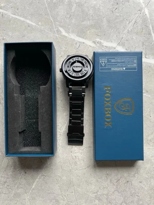 Svart metallklocka från FOXBOX. Price is negotiable - Stilren svart klocka från FOXBOX med metallarmband och urtavla med romerska siffror. Klockan har en modern design med tydliga detaljer och levereras i originalförpackning. Perfekt accessoar för dig som gillar en clean look. Price is negotiable