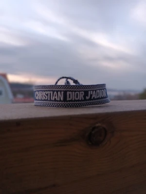 Christian Dior J'Adior tygarmband - Säljer ett snyggt Christian Dior med texten 'J'Adior' armband i vit med blå. Armbandet har en enkel och trendig design med justerbar knytning. Perfekt accessoar för att lyfta din outfit med en exklusiv och grisch touch.