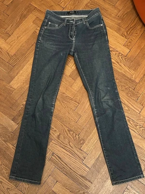 Mörkblå bootcut jeans med brodyr - Säljer ett par mörkblå bootcut/straight jeans med vita kontrastsömmar och snygg brodyr på bakfickorna. Klassisk femficksmodell med dragkedja och knapp. Jeansen är tillverkade i denim med stretch. De är köpta secondhand men använda ett fåtal gånger, alltså är de i bra skick.