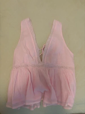 Ljus rosa topp  - Supersöt ljusrosa topp med djup v-ringning och spetsdetaljer längs kanterna. Toppen har snörning i ryggen vilket gör den justerbar. 