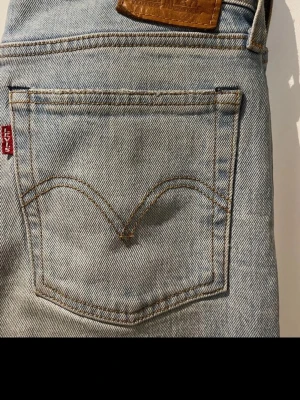 Ljusblå jeans från Levi's - Säljer ett par klassiska ljusblå jeans från Levi's med rak passform och hög midja. Jeansen har fem fickor, Levi's ikoniska röda etikett på bakfickan och är gjorda i slitstark bomullsdenim. Perfekta till en avslappnad stil.