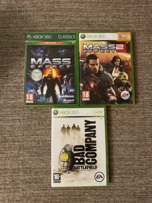 Xbox 360 spel: Mass Effect & Battlefield - Tre Xbox 360-spel: Mass Effect, Mass Effect 2 och Battlefield: Bad Company. Alla i sina originalgröna plastfodral med tryckta omslag. Spelen är från BioWare och EA, och har tydliga åldersmärkningar på framsidan.