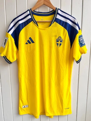 Sverige - Matchtröja 2026 - Player version (XL) - Säljer en svensk landslagströja 2026 (fan version). Tröjan är en reprint i nyskick. Inget namn eller nummer. WC-patches på ärmarna.    Storlek:XL, liknar mer en tajt L/XL