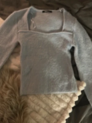 Ljusblå ribbstickad tröja - Trendig ljusgrå stickad tröja med ribbad struktur och fyrkantig halsringning. Långärmad modell som passar perfekt till jeans eller kjol. Mjuk och skön.