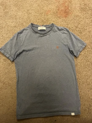 Blå t-shirt från Les Deux - Snygg blå t-shirt från Les Deux med diskret logga broderad på bröstet. Klassisk rund halsringning och korta ärmar. Tillverkad i mjuk bomull som känns skön mot huden. Perfekt basplagg för en clean och enkel stil.