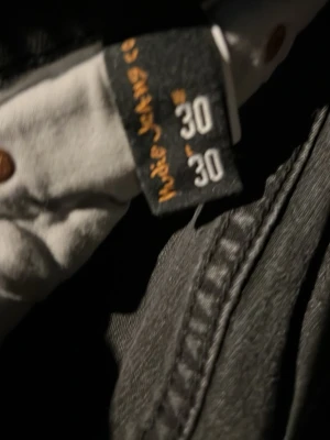 Svarta jeans från Nudie Jeans, W30/L30 - Säljer ett par svarta jeans från Nudie Jeans med klassisk femficksmodell och snygga sömmar på bakfickorna. Jeansen har normal midja och raka ben. Perfekta för dig som gillar en stilren och avslappnad look.