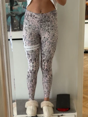 Mönstrade leggings i rosa och grått - Säljer ett par snygga leggings med leopardmönster i rosa, grått och vitt. Byxorna har ett stort vitt amin märke på ena låret. Stretchigt material som sitter tight och bekvämt. Perfekta för dig som vill ha något trendigt och sportigt.