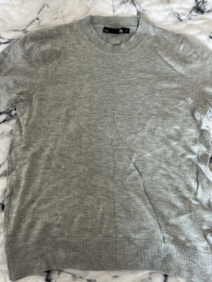 Ljusgrå stickad tröja lager 157 - En enkel och stilren ljusgrå stickad tröja från lager 157. Tröjan har rund halsringning, ribbade muddar vid ärmslut och nederkant samt en mjuk och tunn stickning som passar perfekt till lager-på-lager. Klassisk modell utan mönster.