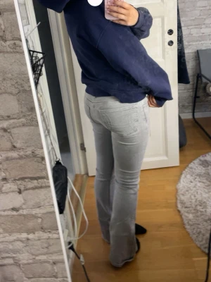 Gråa bootcut jeans - Säljer ett par ljusgråa bootcut jeans med klassisk femficksdesign. Jeansen är low waist och är i stretchigt denimtyg som sitter snyggt.