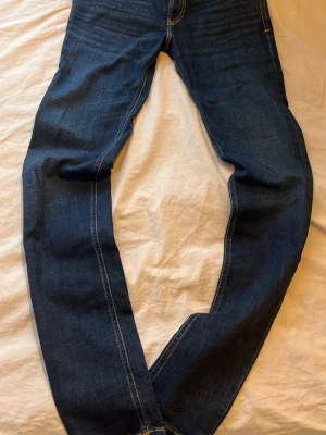 Mörkblå jeans från Diesel - Snygga mörkblå jeans från Diesel med klassisk rak passform och kontrastsömmar. Jeansen har en diskret röd Diesel-logga på bakfickan och är tillverkade i slitstarkt denimtyg. Perfekta för en avslappnad och trendig look. Storlek 30/34.