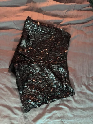 Svarta paljettshorts  - Glittriga/paljett shorts med tight passform och hög midja. Finns ingen lapp på dom men har kunnat ha dom och jag är en storlek M :) 