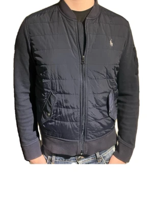 Svart pufferjacka från Polo Ralph Lauren - Snygg svart pufferjacka från Polo Ralph Lauren med quiltad front, två fickor med tryckknappar och en extra ficka med dragkedja på ärmen.  Strl M och kostar ny 4000!