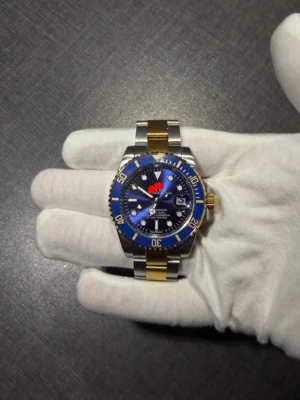 Blå och guld klocka - Stilren klocka med blå urtavla, gulddetaljer och silverfärgad samt guldfärgad länk i metall. Klockan har tydliga index, datumvisning och vridbar bezel i blått och guld. Perfekt accessoar för dig som gillar en lyxig look.