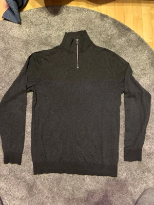 Mörkgrå stickad tröja Jack & Jones - Mörkgrå stickad tröja från Jack & Jones med hög krage och halv dragkedja framtill. Tröjan har långa ärmar och ribbade muddar vid ärmslut och nederkant. Perfekt för lager på lager och enkel att matcha till olika outfits.